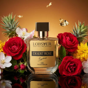 Lobster Desert Rose perfume bottle surrounded by flowers on a reflective surface with a warm brown background.
